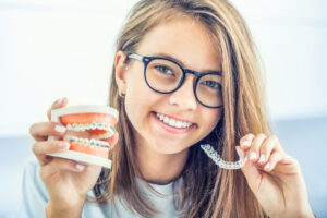 Blonde woman holding two mouth models, one with Invisalign® and one with metal braces
