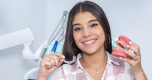 Happy young woman holding a mouth with braces in one hand and a clear aligner in the other